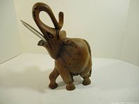 Front-quarter view of wooden elephant statue showing detailed trunk, tusks, and painted accents on ears and body.