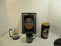 Full lot showing framed Guinness mirror, glass mug, ceramic mug, and Guinness can bank.