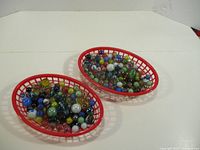 Two red plastic oval trays filled with assorted colorful glass marbles.