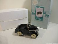 Full view of the black 1937 Ford pedal car model next to original styrofoam packaging and Hallmark box with label.