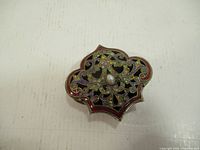 Top view of metal trinket box showing detailed enamel cut-out lid design with central faux pearl-like stone.