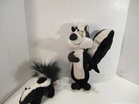 Front view of two black and white skunk stuffed toys including Peppy Lapew and a smaller skunk plush