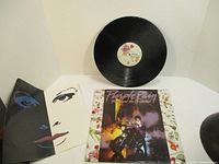 Vinyl record with white center label, album cover, and two illustrated inserts with artistic faces.
