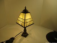 Full view of the lamp showing the stained glass shade illuminated and metal base with cord and switch visible.