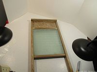 Full view of vintage wooden washboard with glass scrubbing surface laid on white background and two black lamps.
