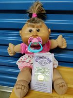Cabbage Patch Kids Veronica doll dressed in pink holding a birth certificate and a pacifier in mouth