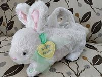 Side view of the white bunny basket plush showing pink ears, green ribbon with heart tag, and carry handle.