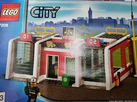 Box front with Lego City Fire Station set 7208 showing fire station building with garage doors labeled 01 and 02, and city skyline background.