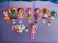 Nine colorful Lalaloopsy mini dolls and seven small plush pets arranged on a blue and lavender background.
