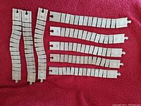Photo of 8 white bendy adjustable plastic toy train tracks on red background, including 2 wider and 6 narrower tracks.