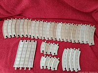 Photo showing various curved and straight white plastic train track pieces in multiple sizes laid out on a red cloth.