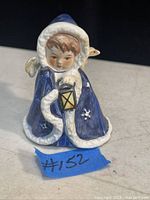 Porcelain figurine of a child wearing a blue winter cloak with white fur trim holding a lantern.