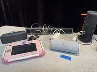 Wide view showing the pink and white VTech InnoTab kids tablet along with four speakers and charging cables on a white surface.