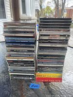Photo showing two stacks of various music CDs on a glass table outside, some visible titles include Elvis Presley, Bon Jovi, Creed, Aerosmith.