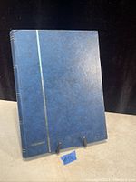 Photo of blue Wartburg brand hardcover stamp album on stand against black background