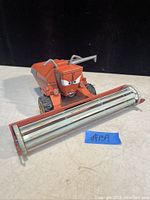 Photo showing front angled view of the orange metal Disney Pixar farm harvester truck toy with expressive eyes and front roller attachment.