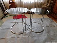 Two round chrome and smoked glass stacking tables side by side on grey backdrop