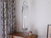 Full view of tall clear glass apothecary jar standing on a wooden table next to a Campbell’s soup can for scale