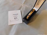 Gold filled bracelet with garnet stones resting inside a black jewelry box with cream satin lining and dark blue velvet insert, showing top and front view with visible garnet stones.