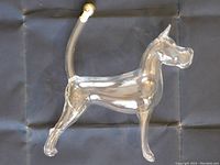 Side view of clear glass dog-shaped decanter on black background showing curved tail with gold-toned stopper.