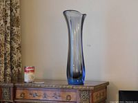 Full view of the tall blue and smoky toned hand blown glass vase on wooden table with a canned soup for size reference.
