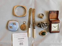 Overhead view of all lot items arranged on grey surface, showing bangle, knives, ring, brooches, locket, box, and clock.