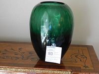 Front view of the green Murano glass vase on a wooden surface with a label in front.