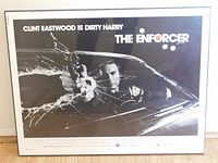 Front view of the black and white movie poster showing Clint Eastwood aiming a gun through a cracked windshield, with title and bullet holes graphics visible