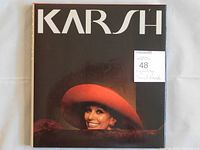 Front cover of 'KARSH' photography book with dust jacket showing title and a color portrait of a woman in a large red hat.