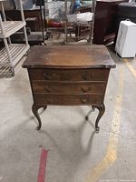 Front view of a dark wooden 3 drawer nightstand with metal handles and curved legs.