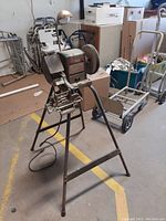 Side and front views of the Craftsman bench grinder mounted on a metal stand in storage area with other equipment.