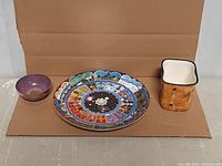 Lot showing all three items: collector plate, brass Tibetan singing bowl, and Sibongile pottery piece