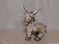 Front right side view of a white concrete donkey statue showing weathered paint and yellow decorative elements.