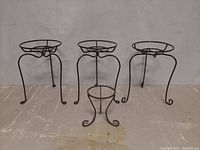 Front view of three larger and one smaller metal plant stands grouped on floor.