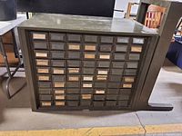 Front view of large vintage industrial metal cabinet with 70 small drawers and label inserts.