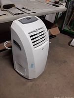 Angled view of white portable AC unit on concrete floor with workshop background