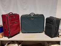 Set of three suitcases side by side: large green hard-shell, large red soft-sided, and medium black carry on all with wheels.