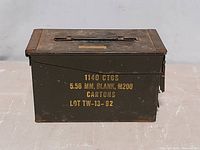 Front and top side view of the metal military ammo can, olive green with yellow stenciled text showing 1140 CTGS 5.56 MM BLANK M200 CARTONS LOT TW-13-92.