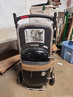 Front view of the closed, folded Weber Traveler portable gas grill with handle upright and secured by a rubber band.