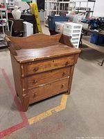 Front angle view of primitive wooden dresser showing 3 drawers and upper raised back and side panels, with visible scratches and wear.