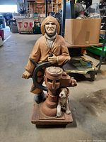 Front side view of the sea captain statue holding the ship's wheel, showing the dog and nautical valve at the base.
