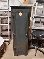 Front view of a tall, narrow, dark-finished pantry cabinet with a single door and round knob.