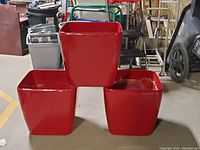 Three large glossy red square planters arranged on the floor showing their shape and size.