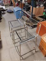 Two chrome and lucite counter stools placed side by side, showing clear seats and backs with chrome tubular frames.
