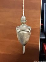 Close-up photo of vintage brass plumb bob hanging from string showing pointed tip and rounded top with brass finish.