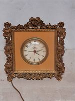 Front view of vintage Globe electric clock with ornate gold-tone floral frame and round clock face with Arabic numerals.