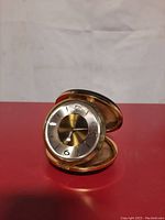 Front view of vintage Seth Thomas alarm clock with silver and gold-tone dial inside brass casing, open black leather foldable case.