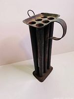 Side view showing six cylindrical cavities and a curved handle of the antique metal candle mold.