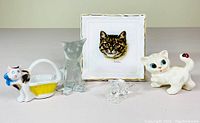 Front view of six cat-themed porcelain and glass pieces including 5 figurines and one decorative plate with cat face illustration