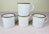 Four white stoneware coffee mugs arranged in two layers showing size and rim detail with brown trim.